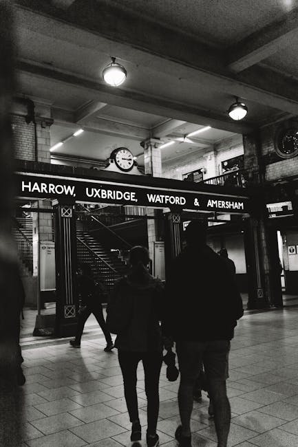 A nighttime exterior view of Uxbridge tube station entrance featuring a prominent roundel sign with red, blue, and white colours displaying the London Underground logo. Adjacent to the station, there